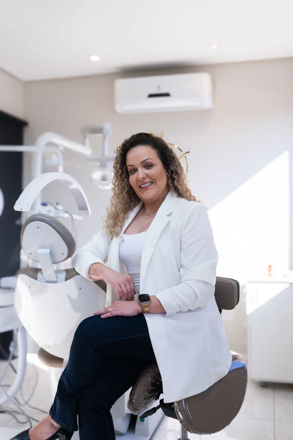 Dra. Jessica Koch sorrindo, sentada ao lado da cadeira odontológica do consultório