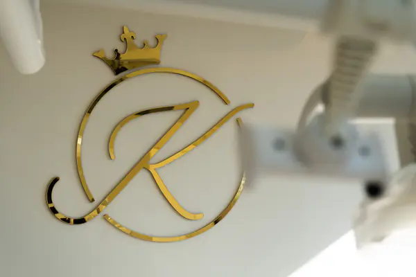 Detalhe do monograma dourado K na parede da sala de atendimento