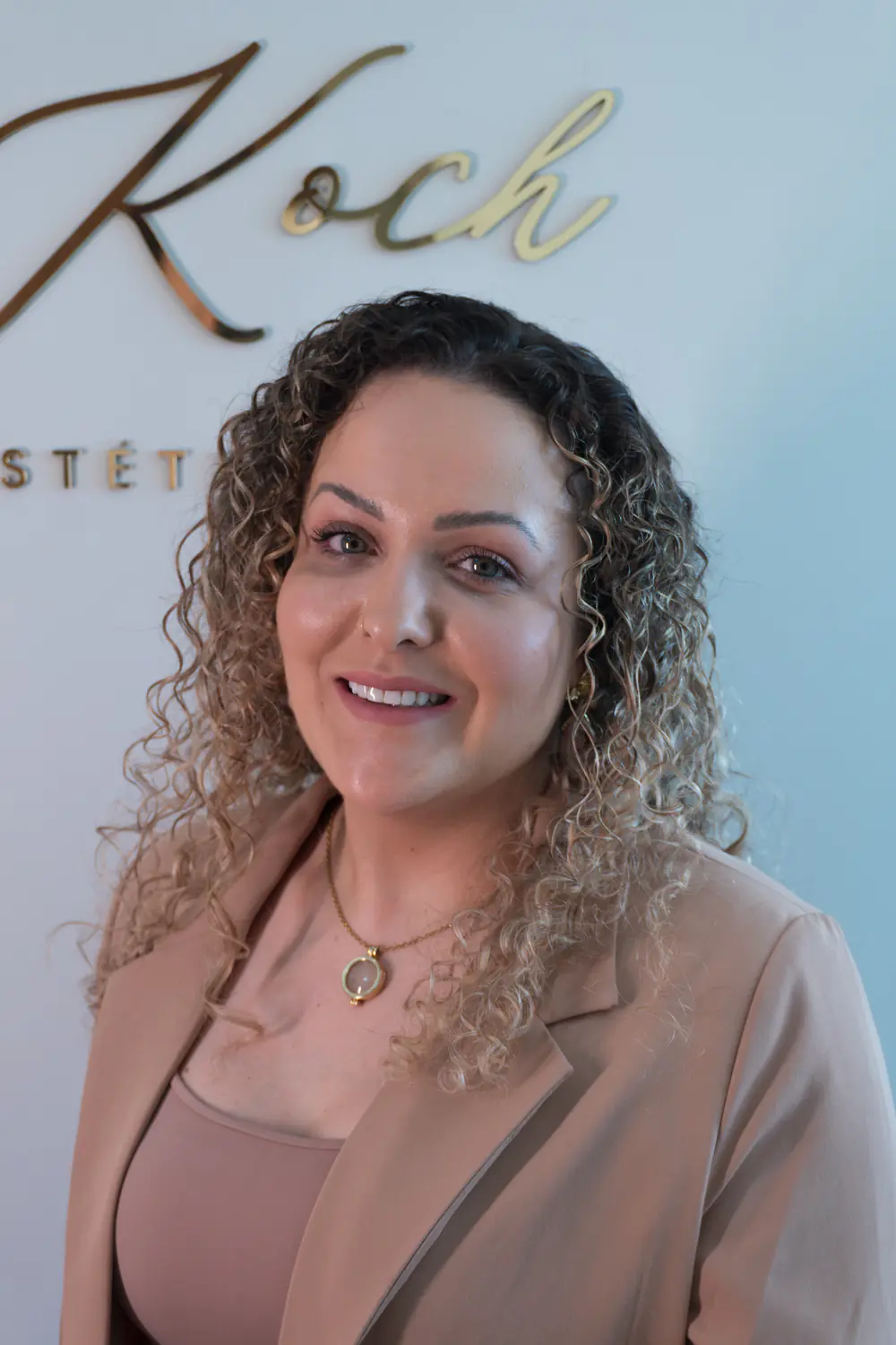 Retrato da Dra. Jessica Koch sorrindo, com o letreiro dourado da clínica ao fundo